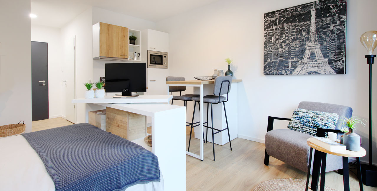 Küche, Essplatz, bequemer Sessel, Beistelltisch und Stehlampe machen die etwas größeren 1-Zimmer-Wohnungen der Kategorie Medium zum wohnlichen Zuhause.
